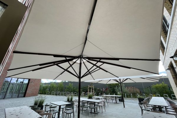 Sonnenschirm Caravita Big Ben in Berlin Abmessung 450x450cm Dokumentation der Montage von Gastro-Sonnenschirmen auf einer Außenfläche eines Gastronomiebetriebs in Berlin. Zu sehen sind Schirmmast, Acryltuch Bespannung und das saubere Ausrichten des Schirms für eine stabile Beschattung.